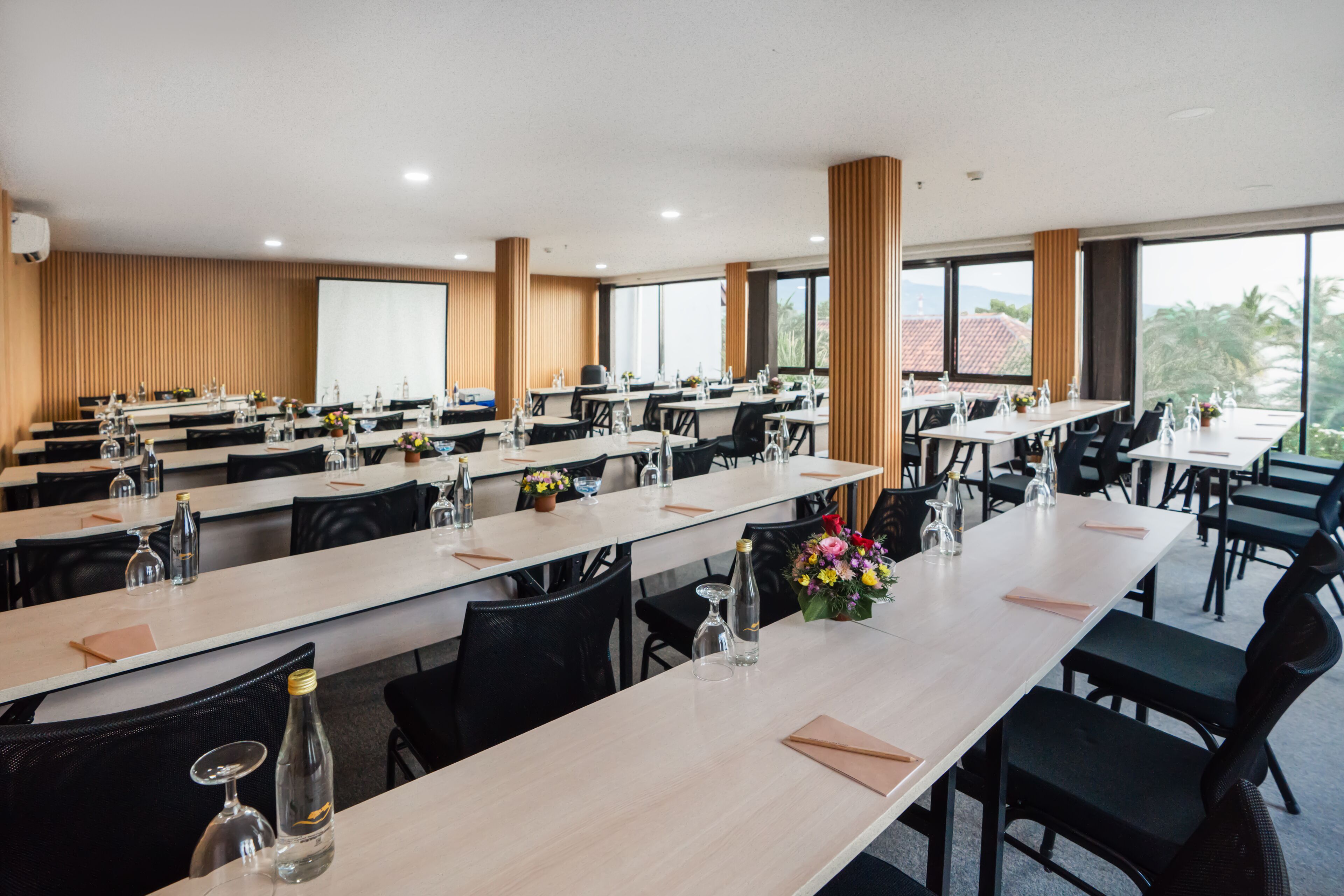 Una sala de conferencias con varias mesas, sillas y una pantalla grande.