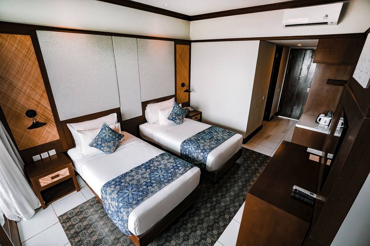 A hotel room with two beds, a desk, a chair, a wardrobe, and a bathroom visible through an open door.