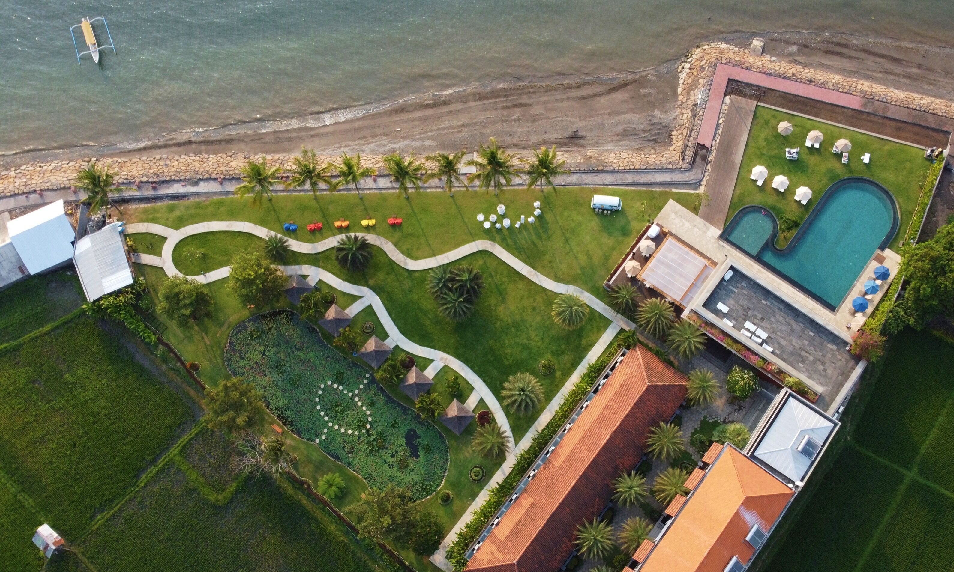 An aerial view of a resort with a swimming pool, a landscaped garden, and a beach area.