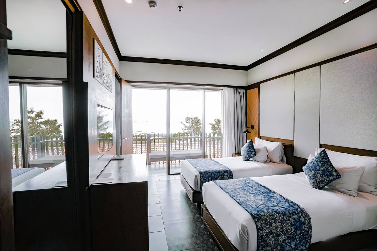 A hotel room with two beds, a balcony, and a large window.