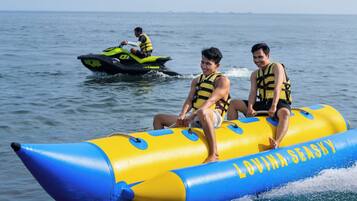 Dos personas en una balsa inflable amarilla y azul con el texto "LOVINA SEASHY". Otra persona está en un jet ski verde al fondo.