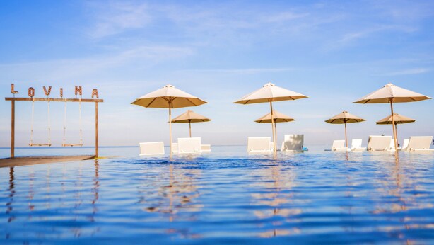 Une piscine à débordement avec des chaises longues et des parasols, et un panneau indiquant « LOVINA ».