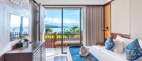 A hotel room with a large bed, a TV, a desk, and a balcony with a view of the sea.