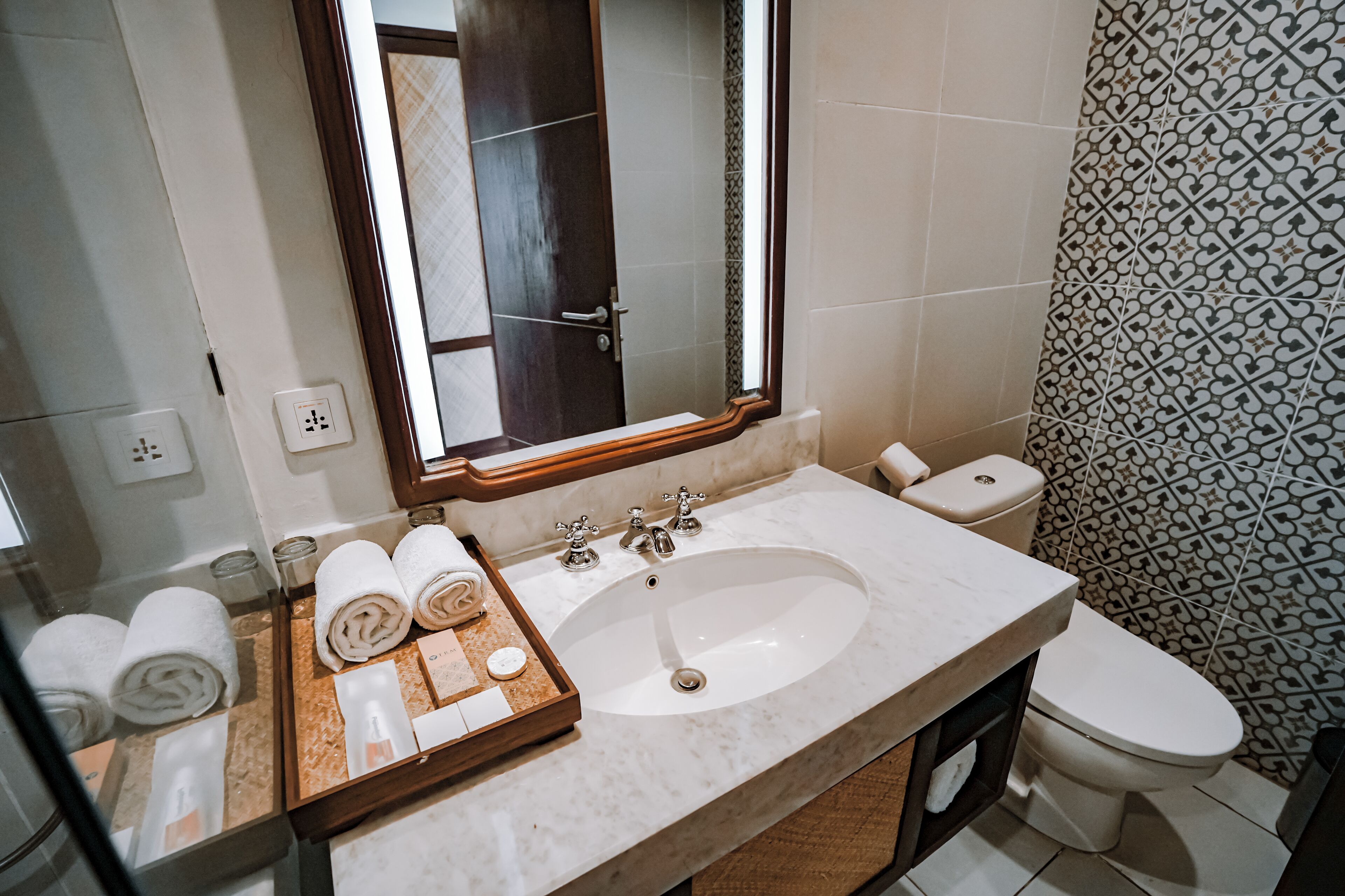 Ein Badezimmer mit Marmorwaschbecken, einem Spiegel, einer Toilette und gefliesten Wänden.