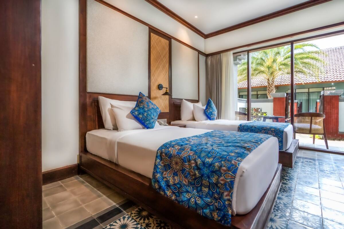 A hotel room with two beds, a large window, and a view of palm trees.