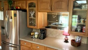 A kitchen with wooden cabinets, a stainless steel refrigerator, a coffee maker, and a lit lamp.