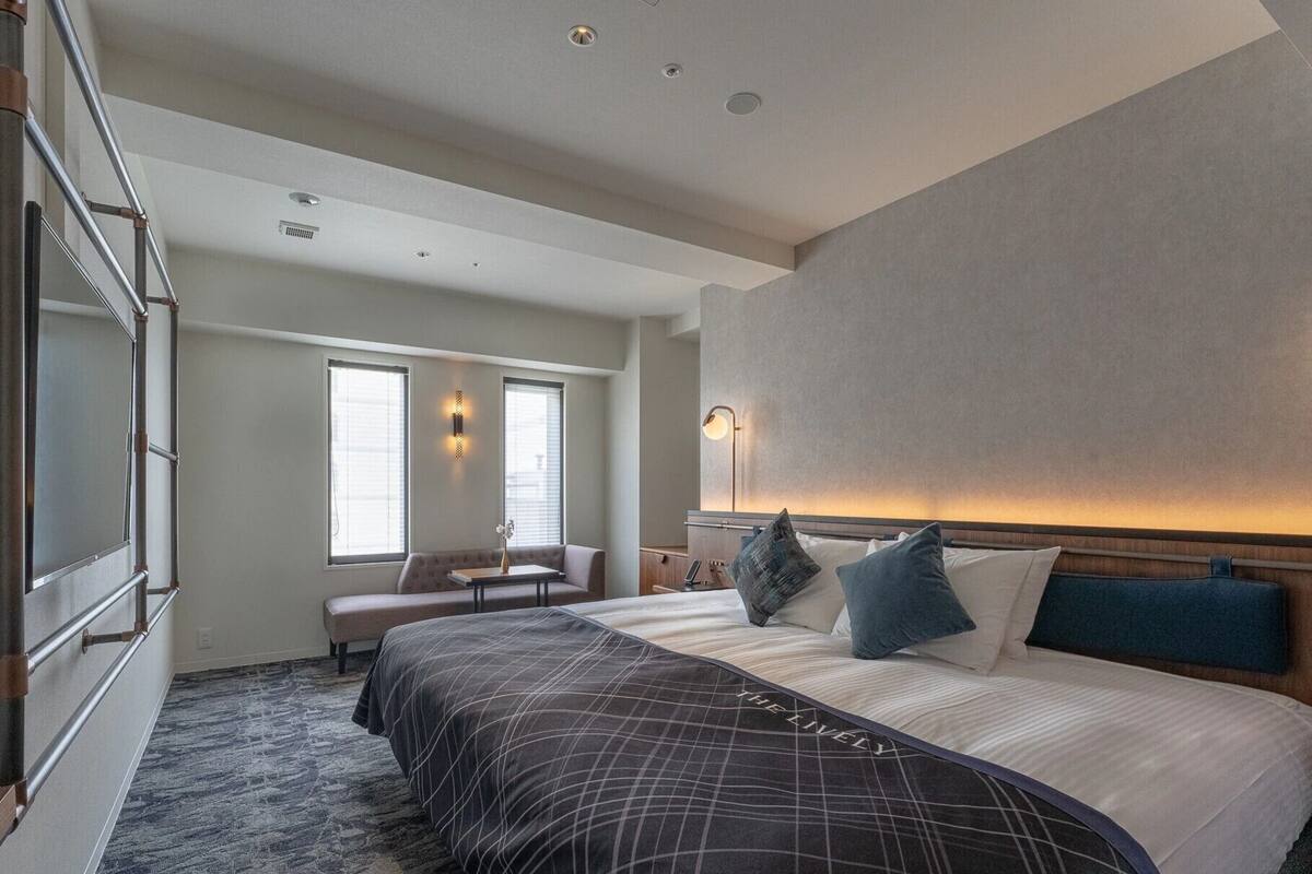A hotel room with a large bed, a seating area with a bench and table, and a wall-mounted light fixture.
