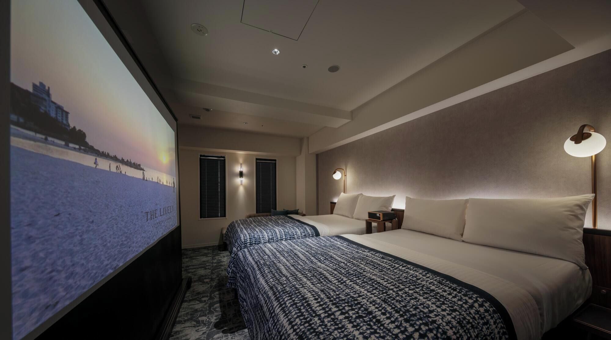 A hotel room with two beds, a large TV screen, and a projector.