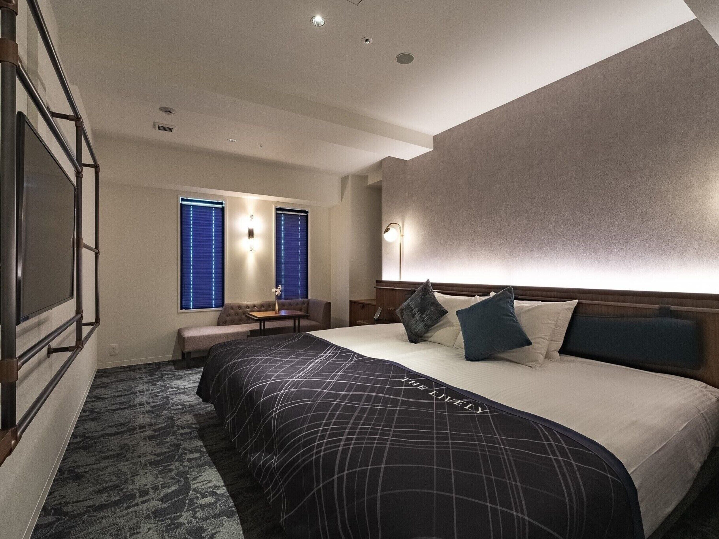 Una habitación de hotel con una cama grande, un área de descanso con mesa y un televisor montado en la pared.