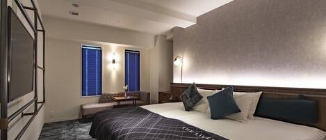 Una habitación de hotel con una cama grande, un área de descanso con mesa y un televisor montado en la pared.