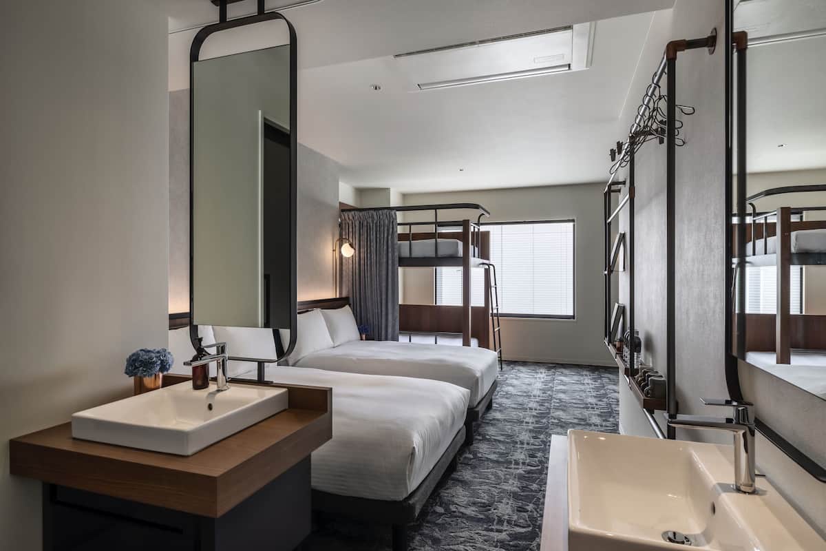A hotel room with a large bed, a smaller bed, a bathroom with a sink and mirror, and a window with curtains.