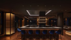 Zona de bar moderna con una isla central, taburetes y un espacio de estar con sofá.