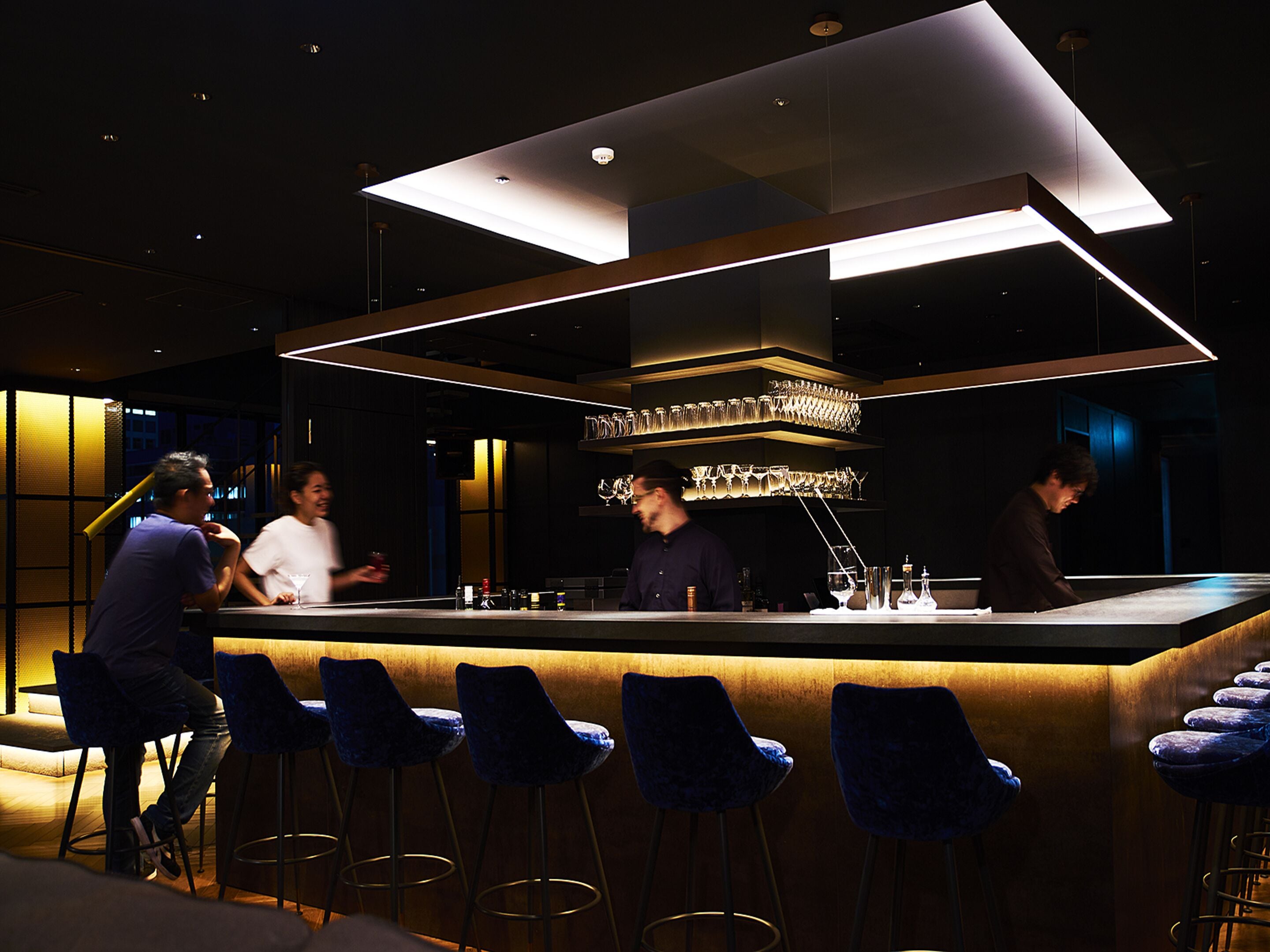 A modern bar area with a bar counter, bar stools, and a ceiling light fixture.