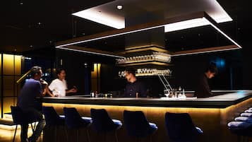 A modern bar area with a bar counter, bar stools, and a ceiling light fixture.
