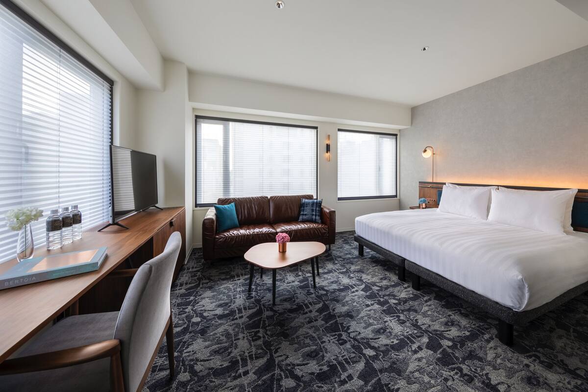 A hotel room with a bed, a desk with a chair, a sofa, a small table, and a TV.