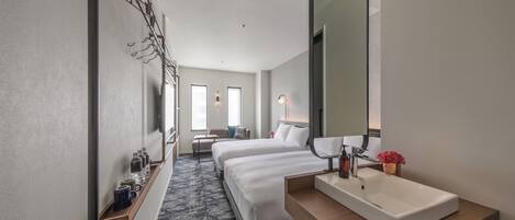 A hotel room with a large bed, a smaller bed, a bathroom with a sink and mirror, and a bench with a view of the hallway.