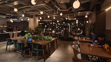 Un café moderno con varias mesas y sillas, algunas con portátiles, y una barra de fondo.