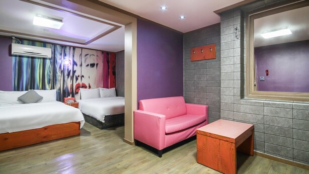 A hotel room with two beds, a pink sofa, and a small wooden table. - Hotel Lie (Geoje)
