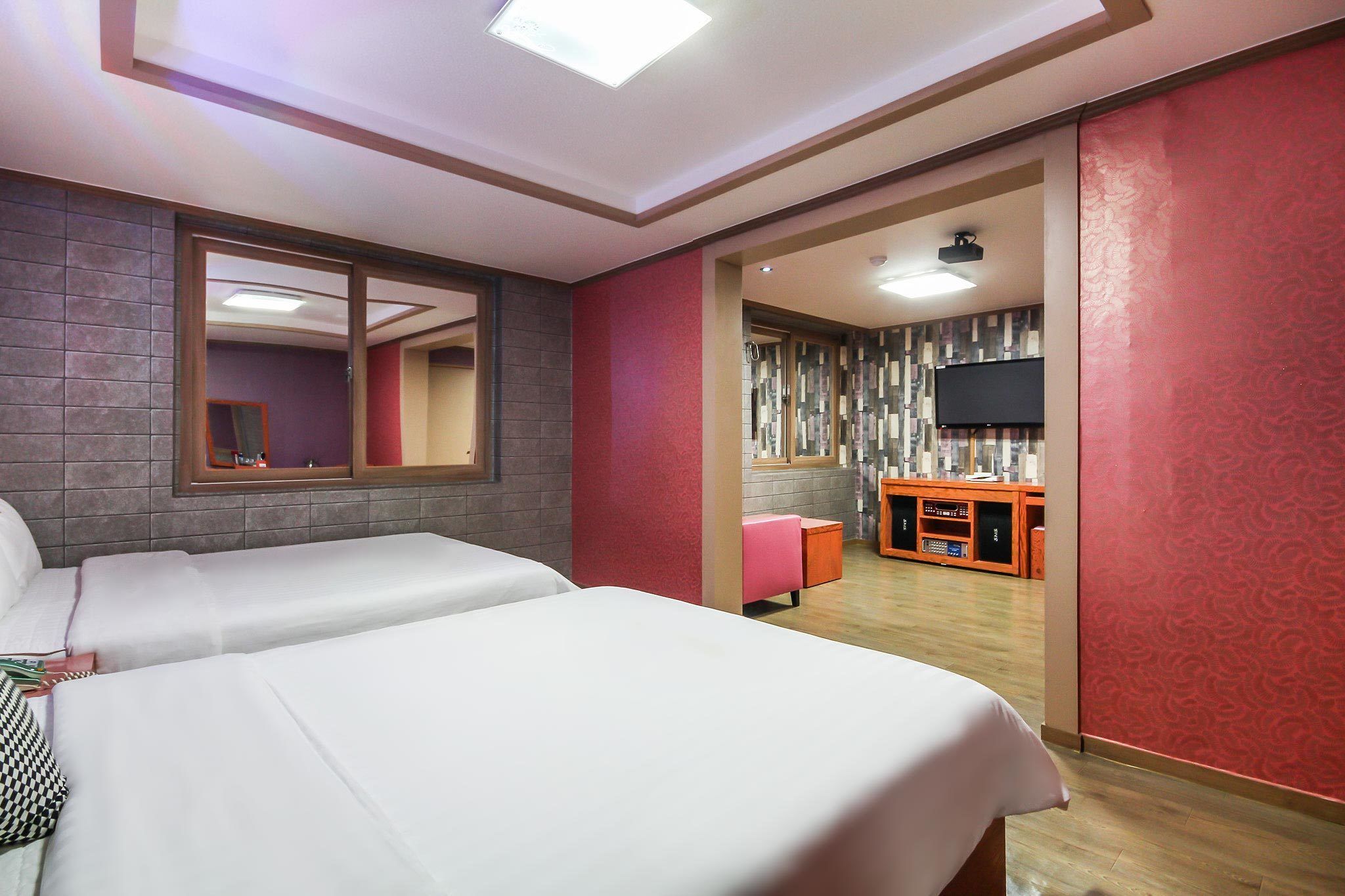 A hotel room with two beds, a TV, a mirror, and a small seating area.