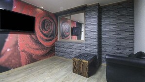 A room with a stone wall, a mounted TV, a wooden ottoman, and a black leather chair. - Hotel Lie (Geoje)