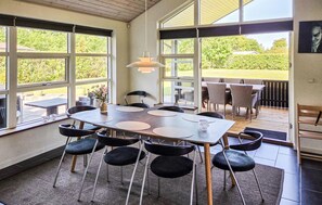 Un espace de restauration intérieur doté d’une grande table et de chaises, de grandes fenêtres et offrant une vue sur l’extérieur.