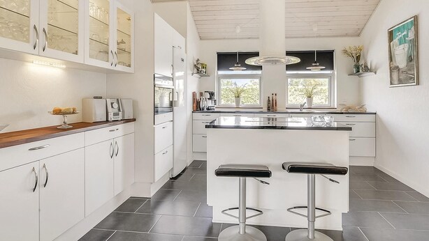 A modern kitchen with white cabinetry, a central island with bar stools, a window with a view, and a ceiling fan. - Stunning home in Storvorde with kitchen (Storvorde)