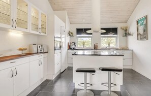 Una cucina moderna con mobili bianchi, un'isola centrale con sgabelli da bar, una finestra vista e un ventilatore a soffitto.
