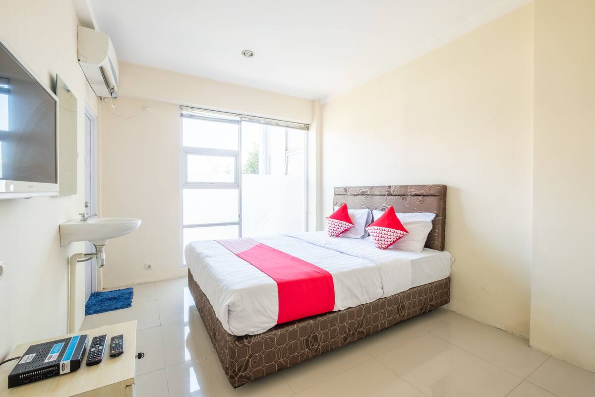 A hotel room with a bed, a TV, a sink, and a window.
