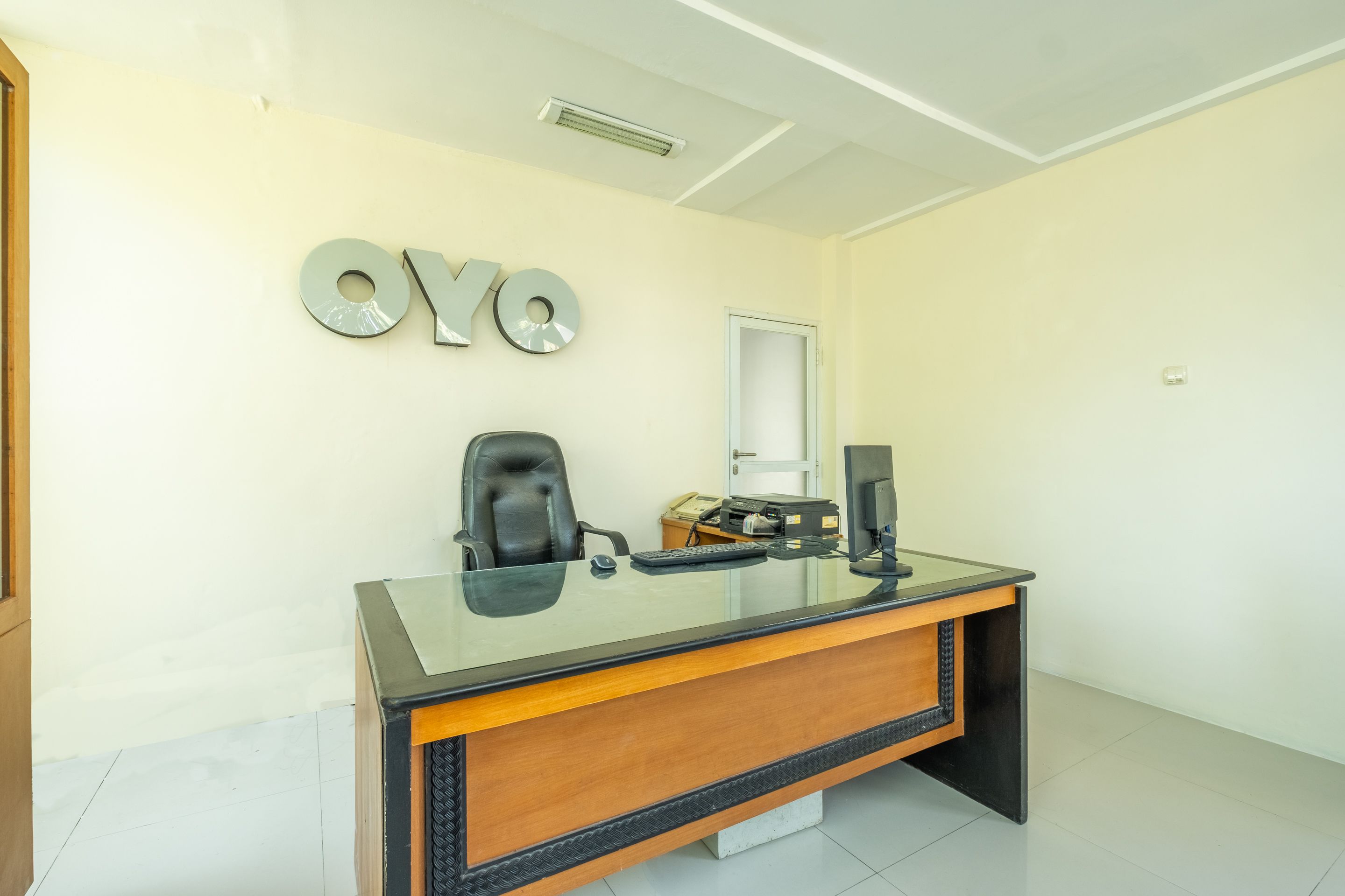A modern office with a glass desk, a black chair, and a wall-mounted sign reading "OYO".