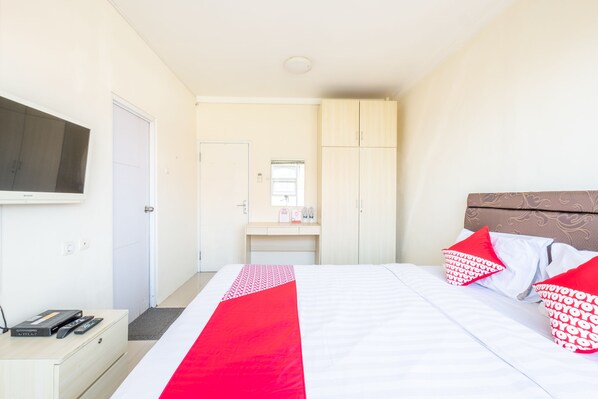 Quarto de hotel com cama, televisão, escrivaninha e armário.