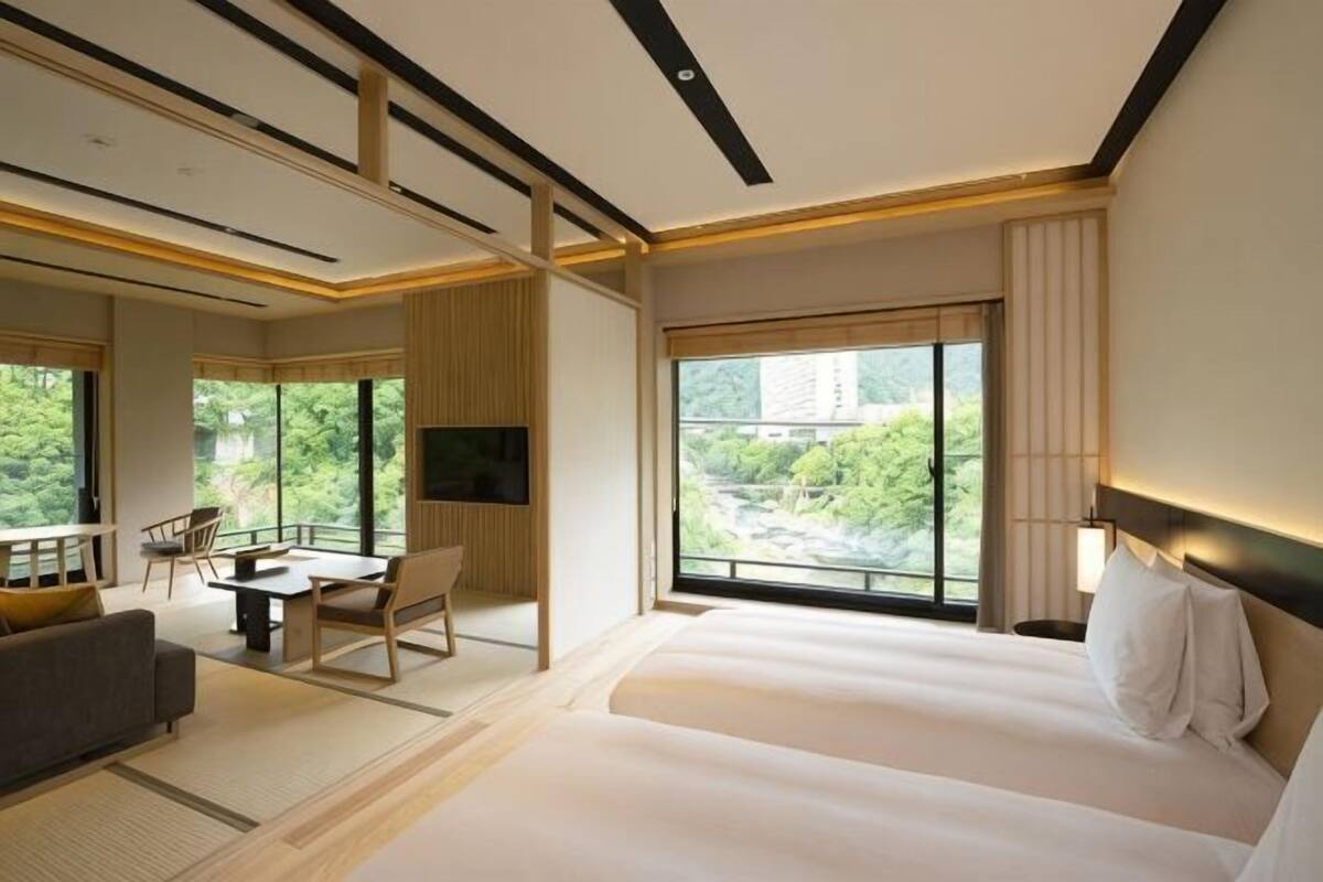 Habitación de hotel con una cama grande, televisión, zona de estar con una mesa y sillas, y vistas a zonas verdes.