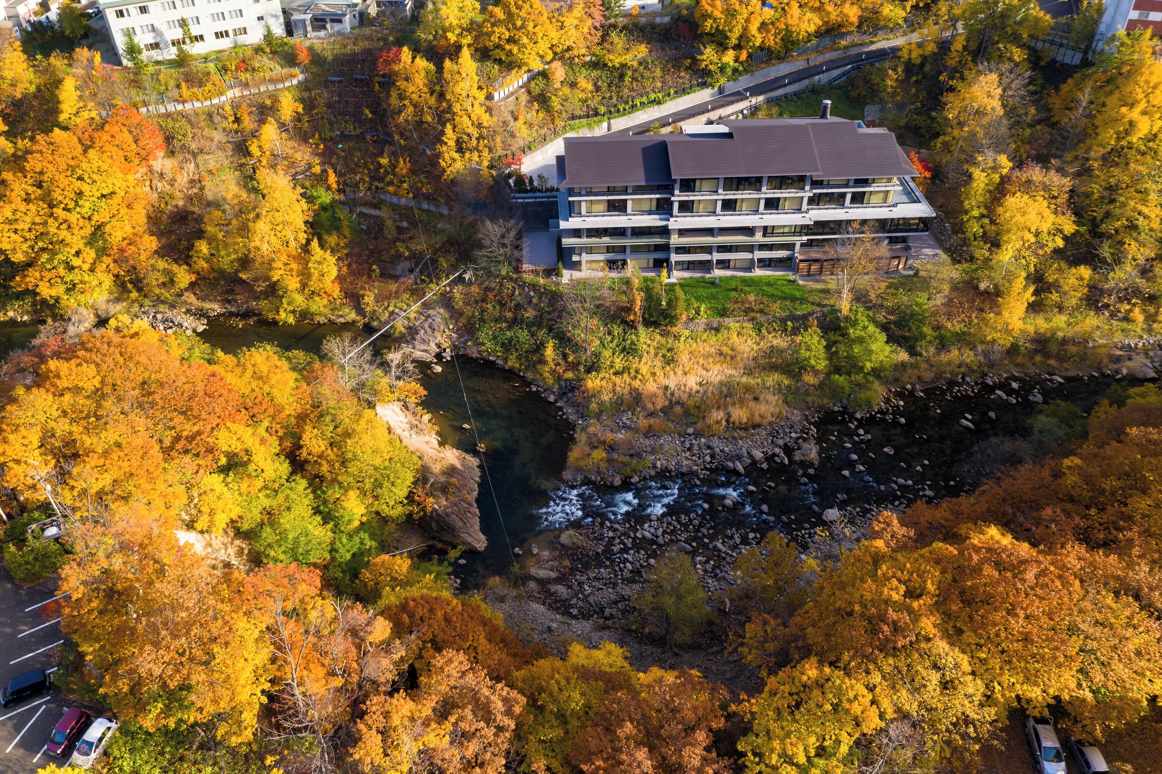 Une vue aérienne d’un bâtiment moderne, entouré d’un feuillage automnal et bordé par une rivière.