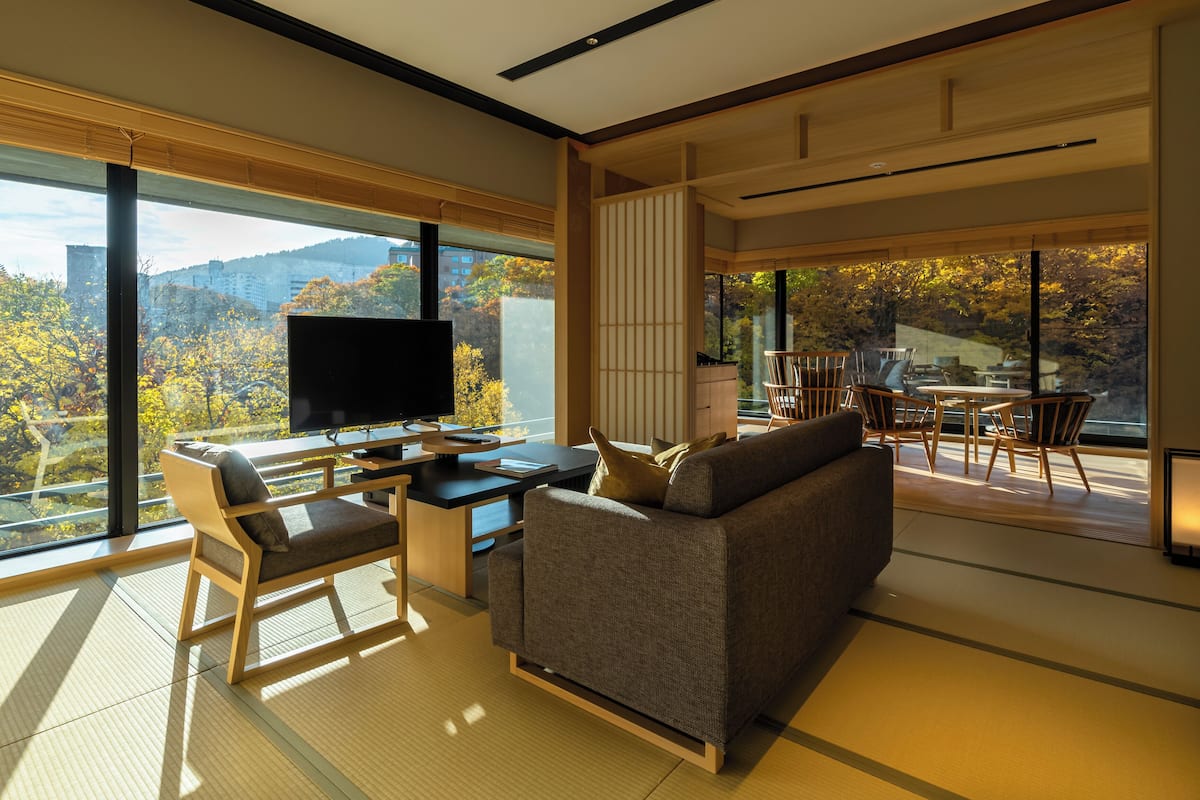 Una sala de estar moderna con un televisor grande, asientos cómodos y vistas del follaje otoñal a través de amplios ventanales.