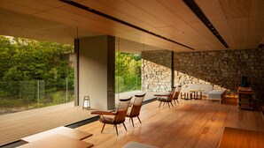 Un intérieur moderne avec un plancher en bois, des murs en pierre et de grandes fenêtres donnant sur un paysage verdoyant.