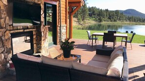 A patio with wicker furniture, a stone fireplace, and a view of a lake and mountains. - Spectacular Waterfront Home in the Mountains.  Welcome to Green Valley Lodge! (Conifer)