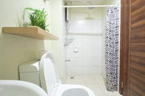 A bathroom with a toilet, a shower, and a wooden shelf with plants.