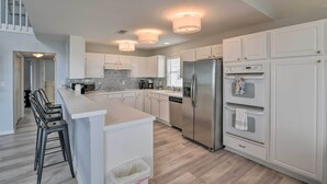 A modern kitchen with white cabinetry, stainless steel appliances, and a central island with bar stools. - Beachside Living: Family Retreat in Galveston (Galveston)
