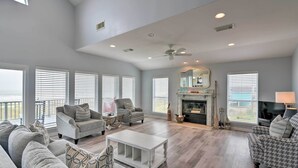 A spacious living room with a high ceiling, large windows, a fireplace, and a balcony. - Beachside Living: Family Retreat in Galveston (Galveston)