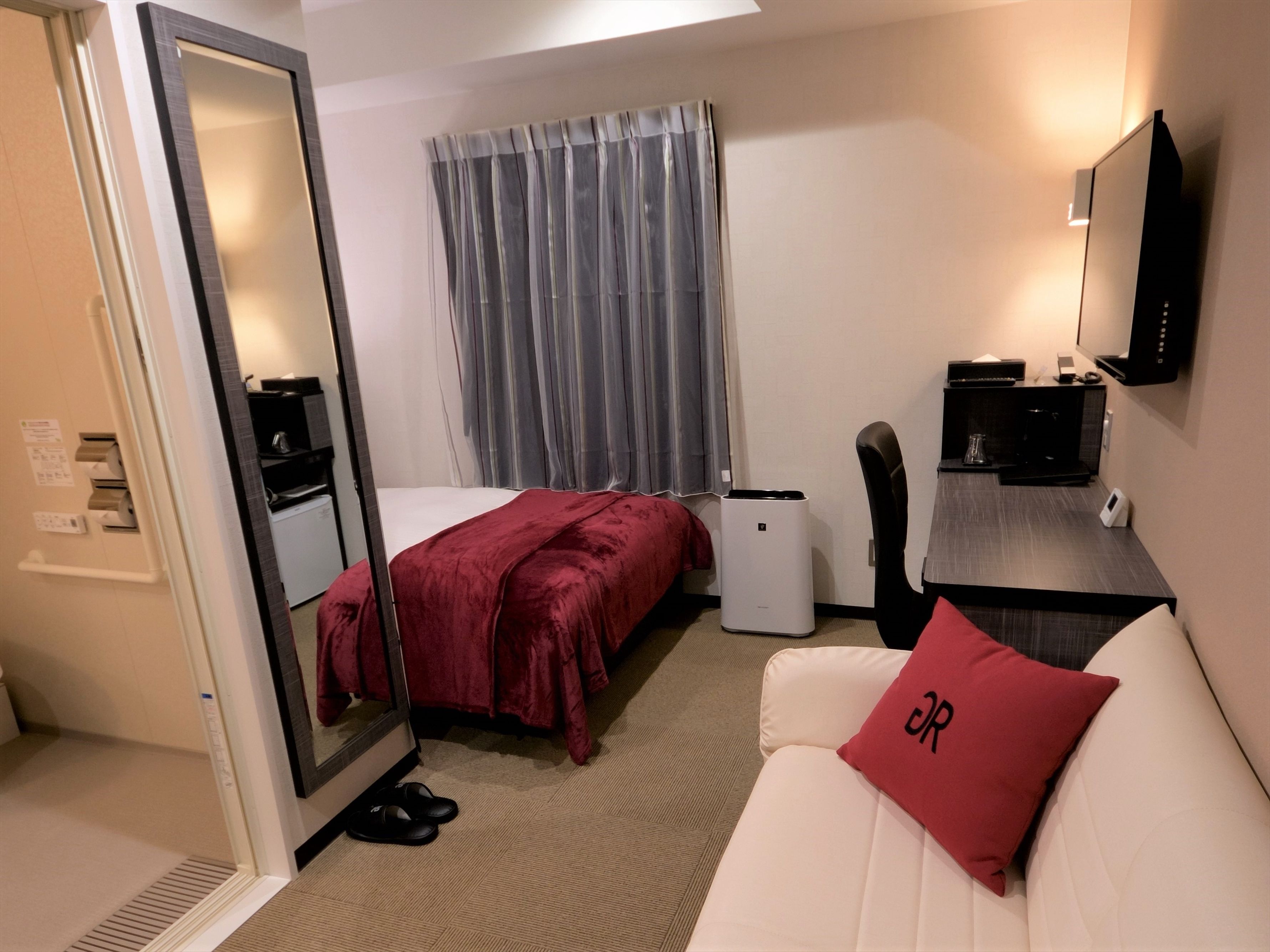 A hotel room with a bed, a desk, a chair, a TV, and a mirror.