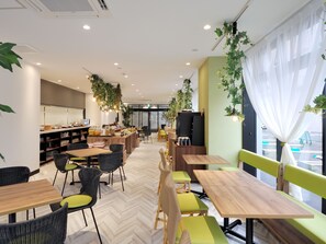 Een modern café met houten tafels en stoelen, een keukenhoek en grote ramen met gordijnen.