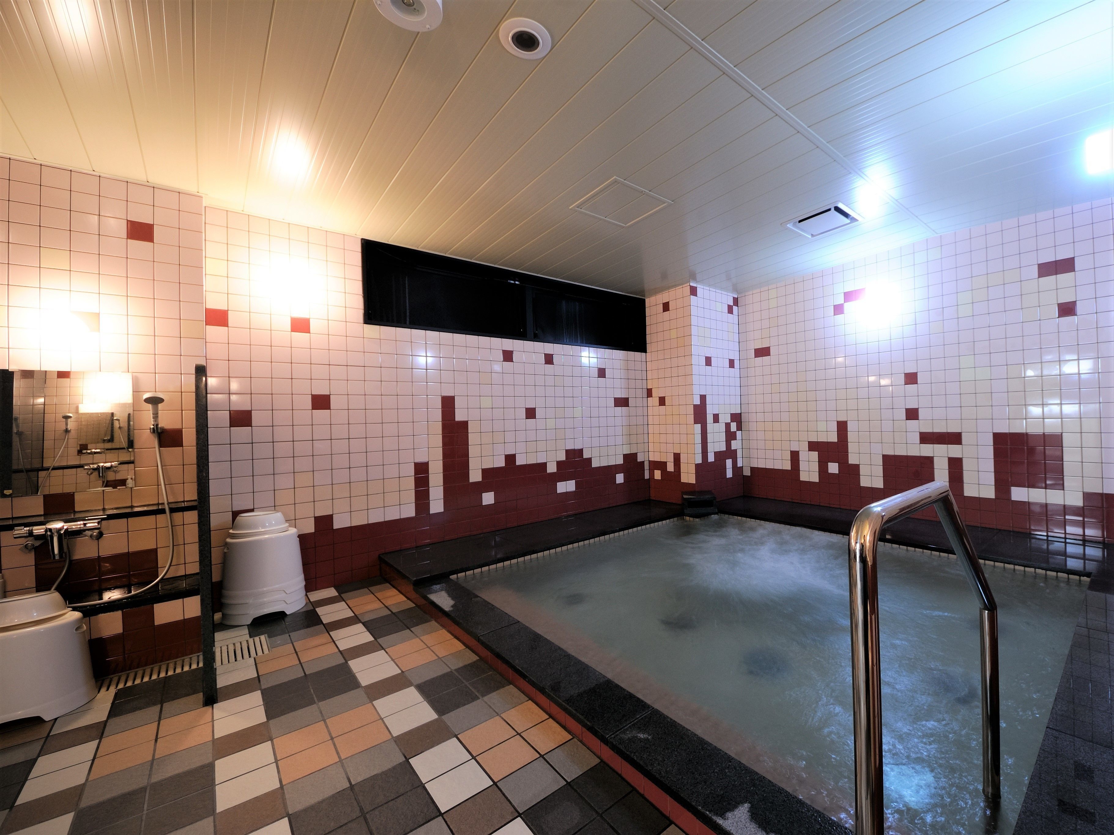 A public bath area with tiled walls, a checkered floor, and a central hot tub.