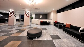 A modern reception area with a check-in desk, seating area, and a central decorative column. - Green Rich Hotel Tottori Ekimae Artificial Hot Spring Futamata Yunohana (Tottori)