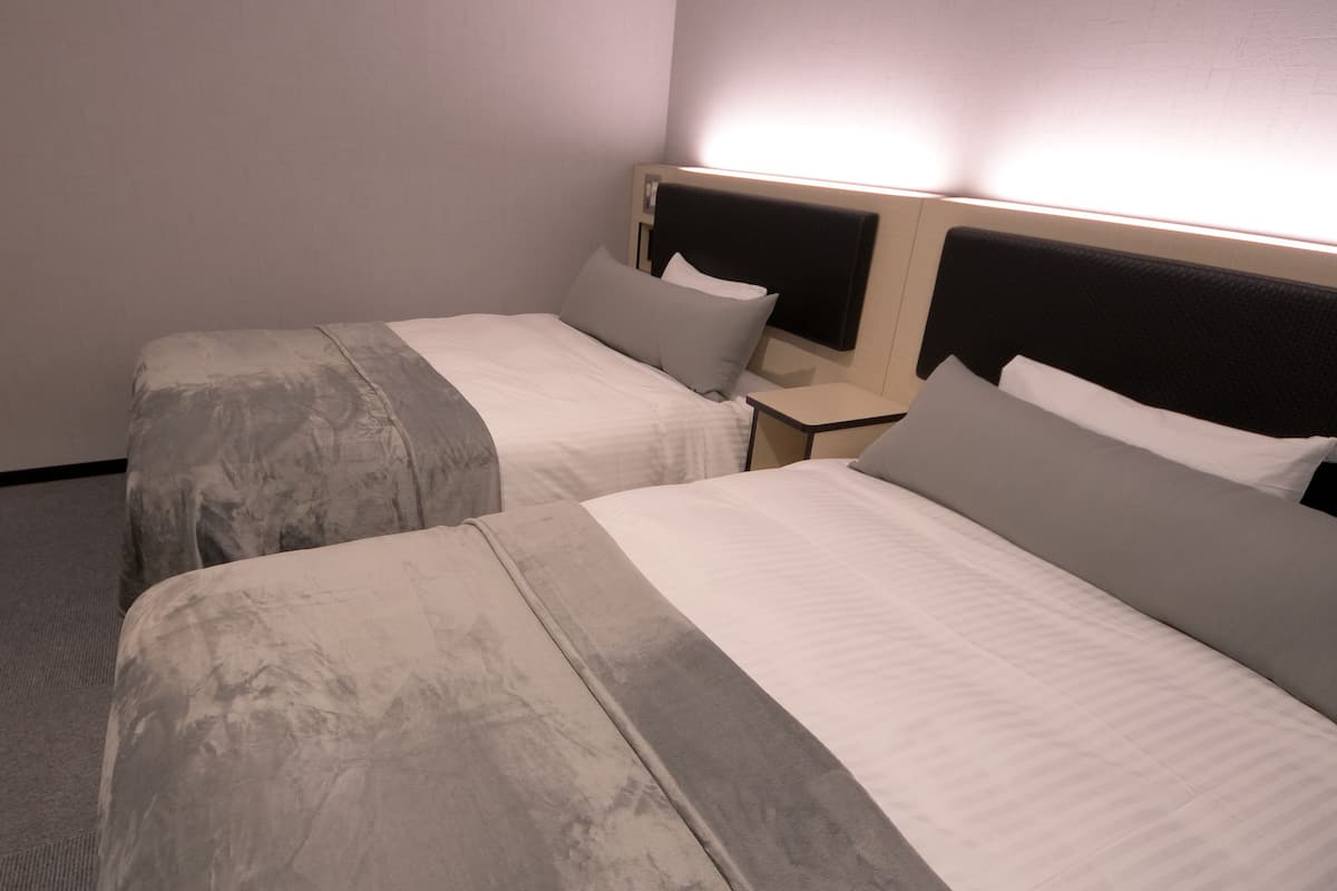 Zwei Einzelbetten mit Kopfteilen, ein Nachttisch und eine Wandleuchte in einem Hotelzimmer.