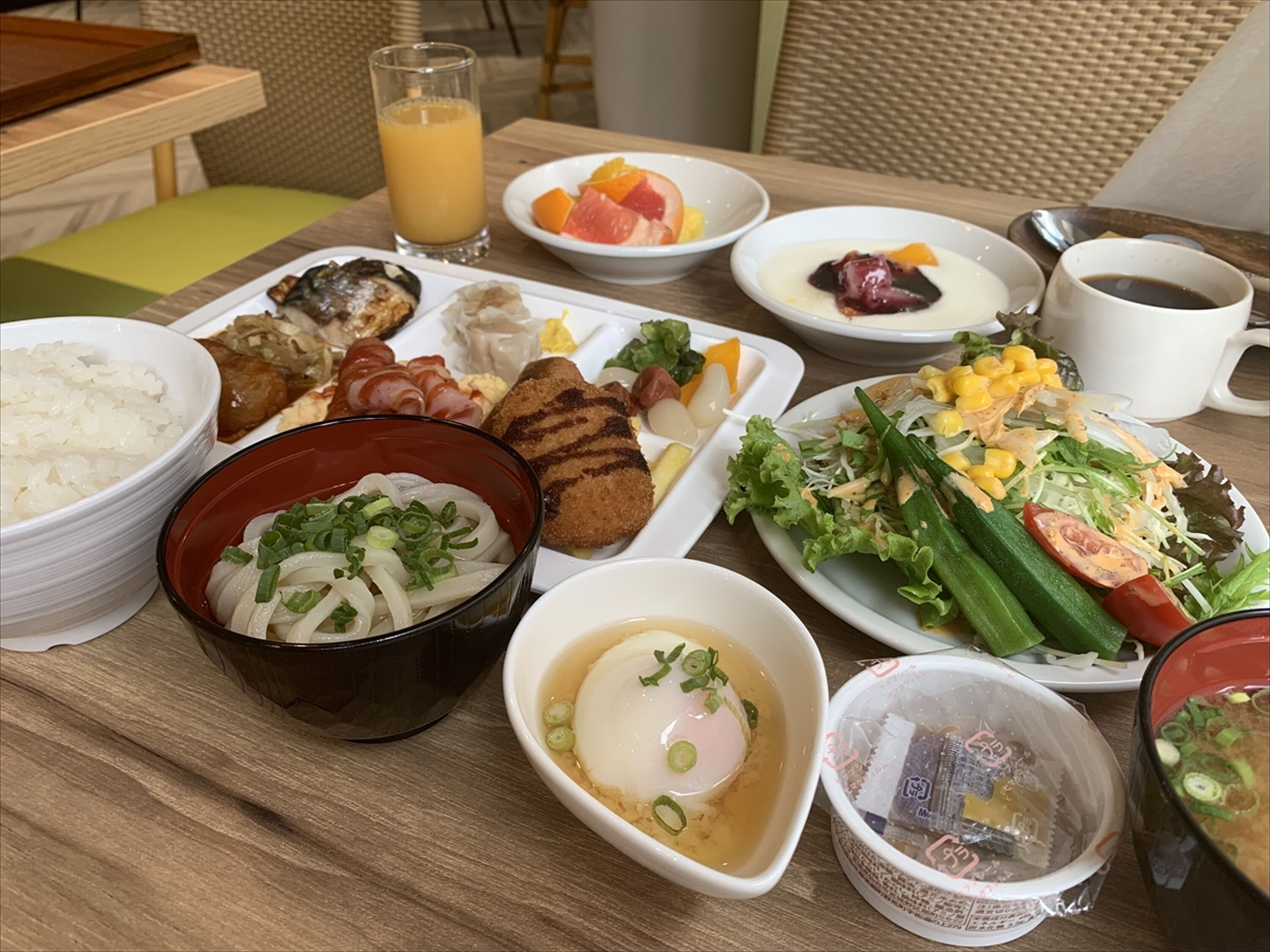 A breakfast table with various dishes including rice, noodles, eggs, and fruits.