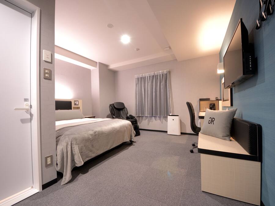 Una habitación de hotel moderna con cama, sillón de masaje, escritorio y televisor.