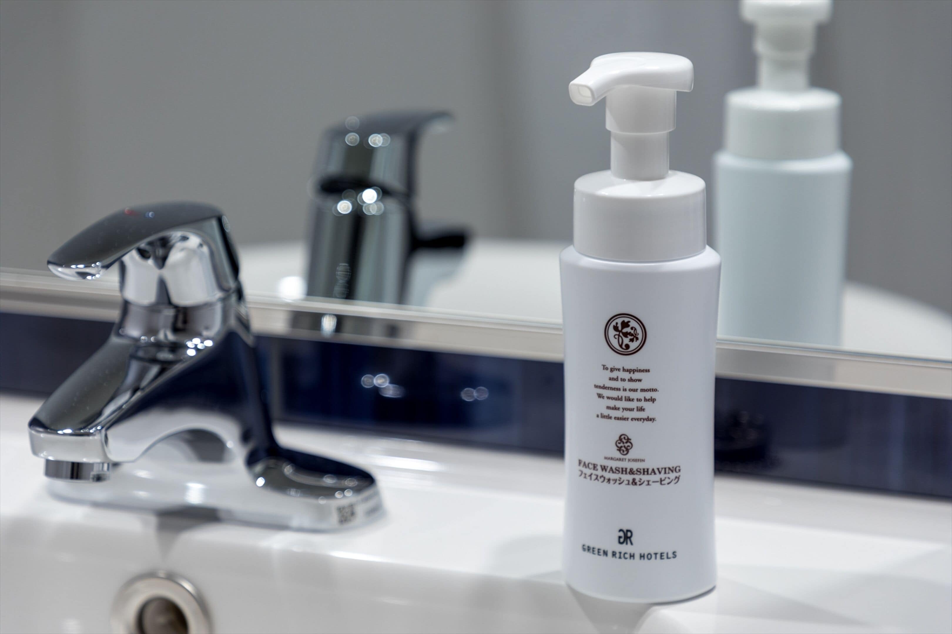 Un lavabo de salle de bain avec un robinet chromé et une bouteille blanche de produit nettoyant pour le visage.