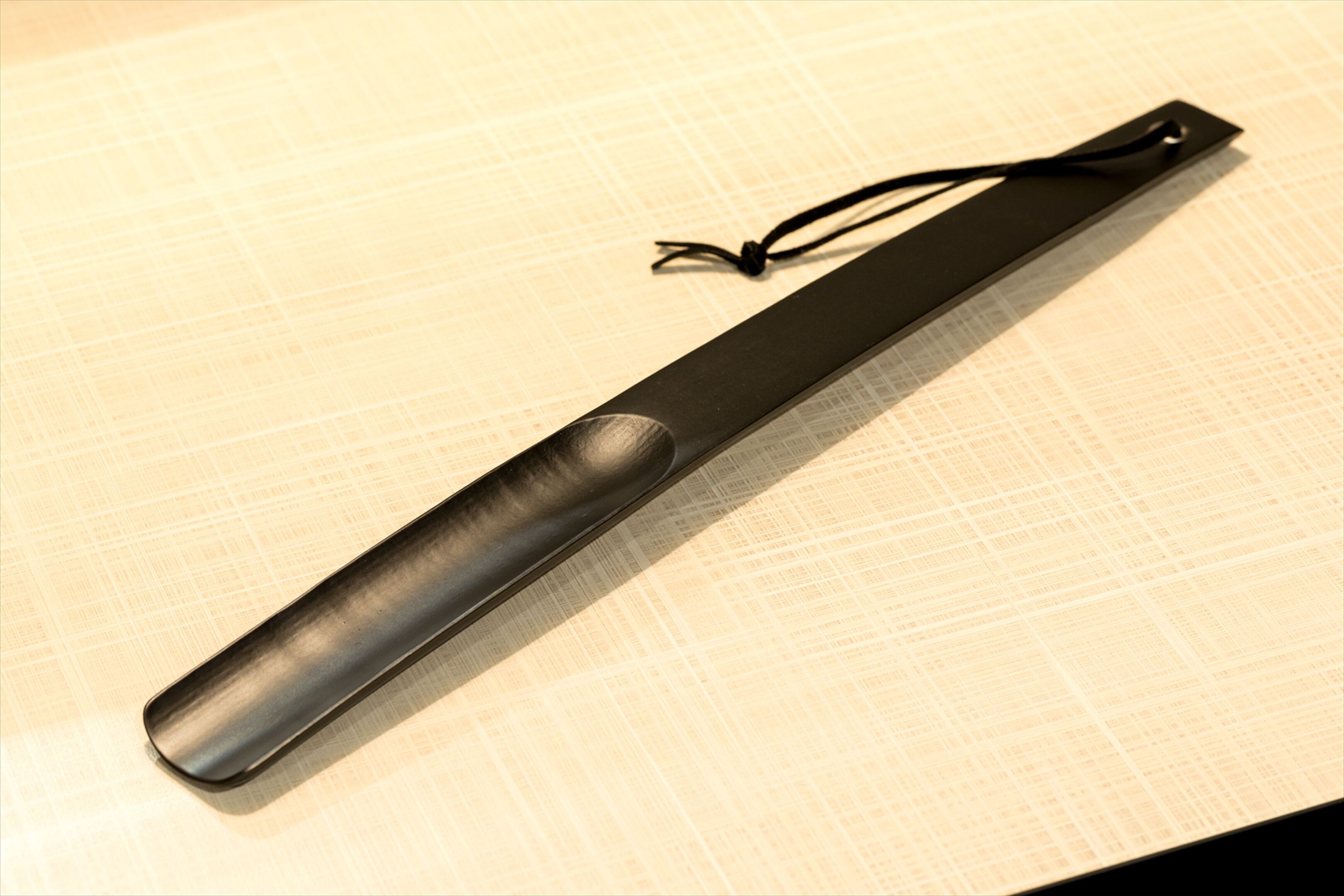 A black object with a textured surface and a cord, placed on a light-colored surface with a grid pattern.
