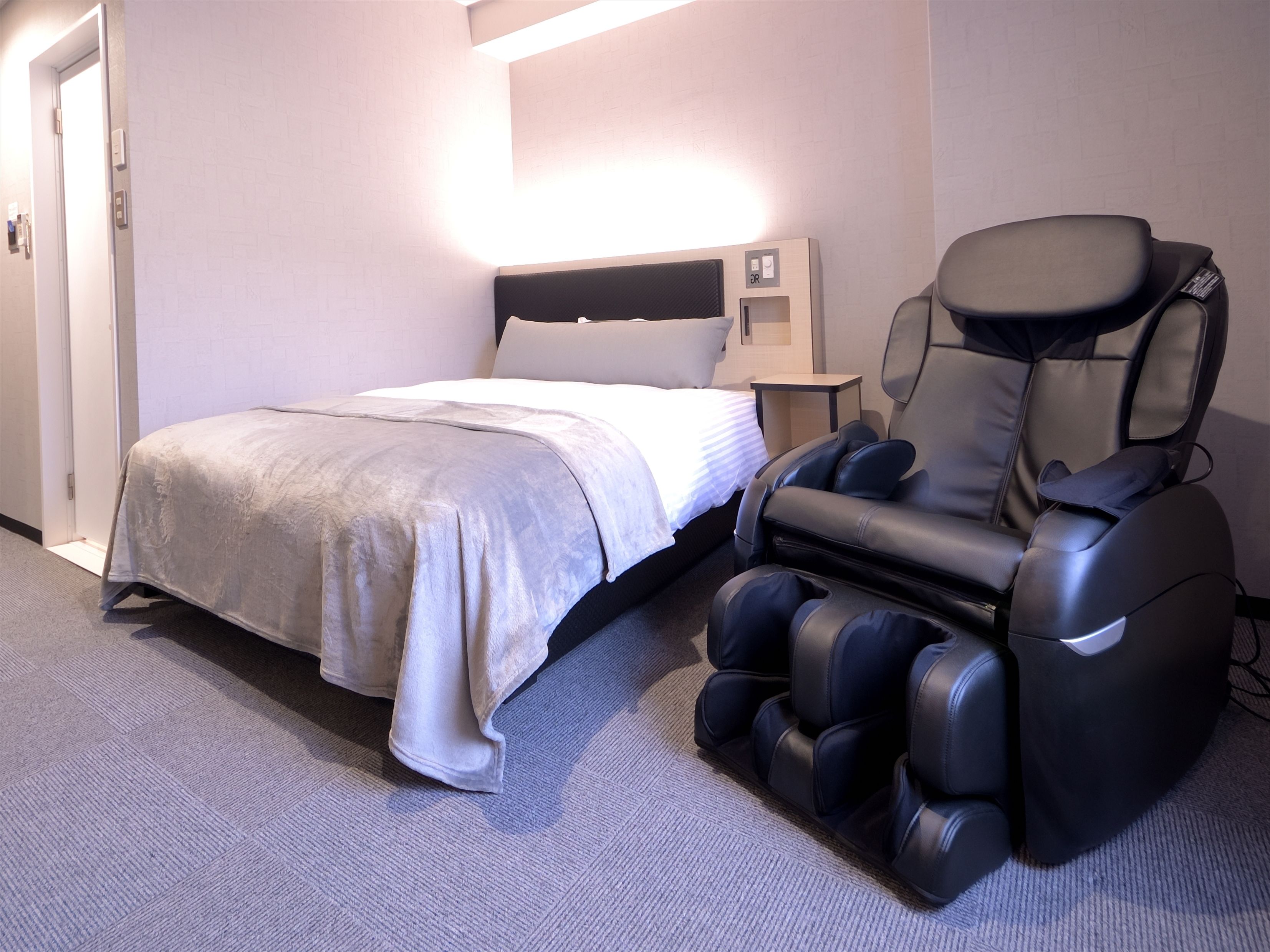 Una habitación de hotel con una cama, una silla de masaje y una mesita de noche.