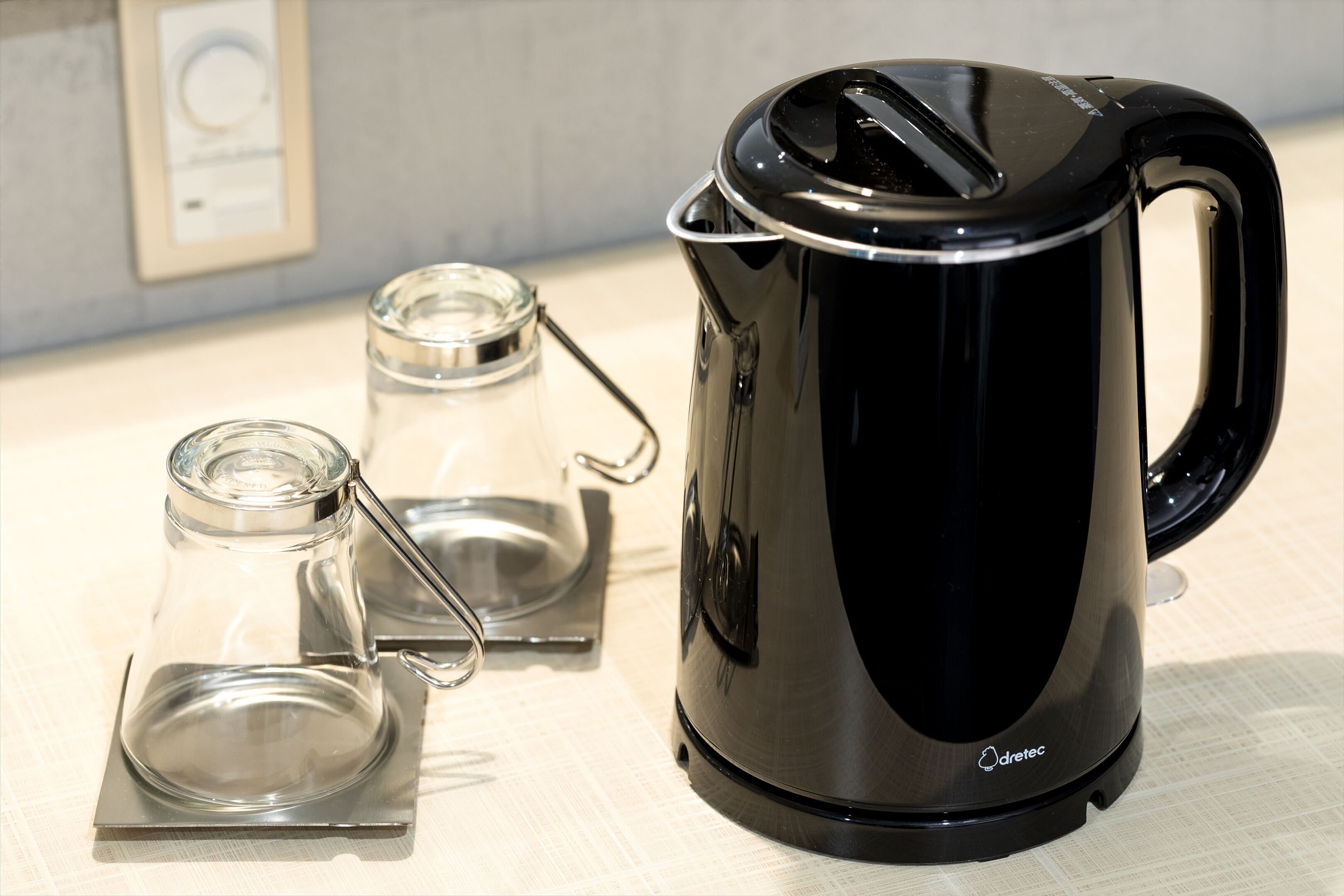 A black electric kettle with a glass carafe and a glass jug on a table.