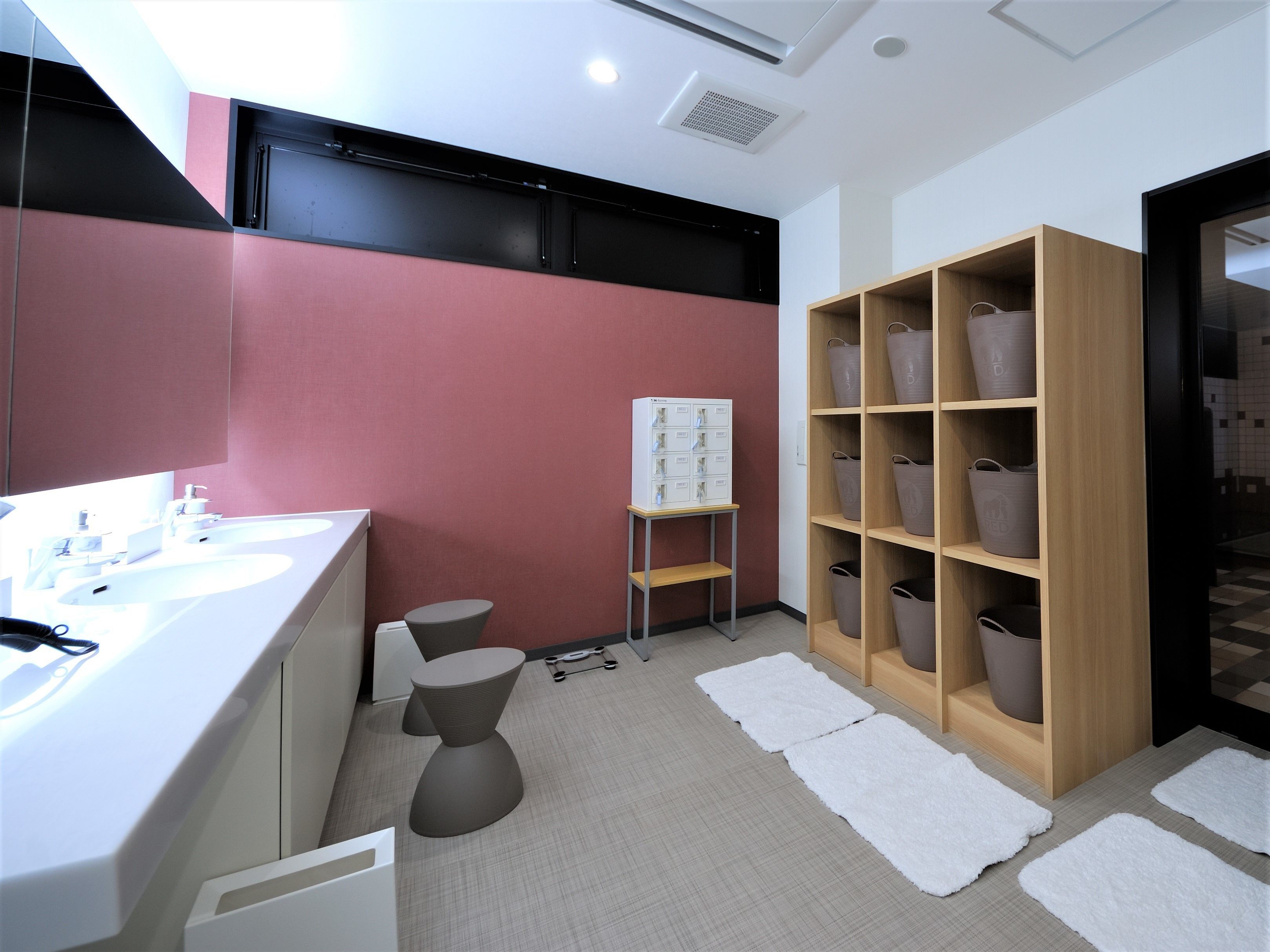 Un baño moderno con un lavabo blanco, un inodoro y un amplio mueble de almacenamiento de madera con cestas.